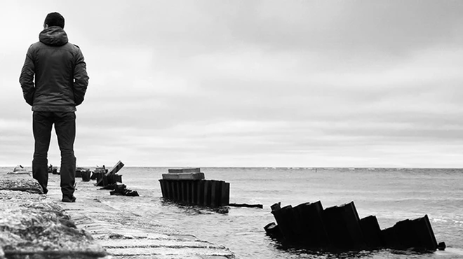Black and white photography of a man by the shore staring at the sea Black and white photography of a man by the shore staring at the sea
