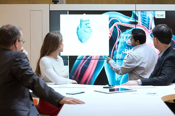 Business people in a meeting room looking at a screen displaying a 3D heart