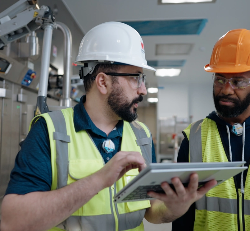 Two employees in hard hats talking in a manufacturing facility 