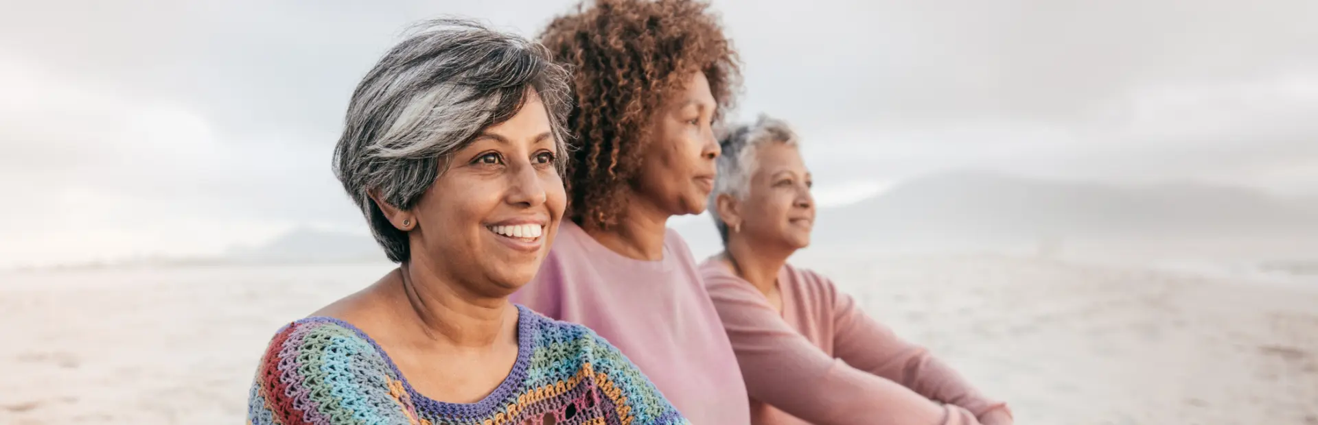 Three women sitting on a beach, looking out at the ocean.