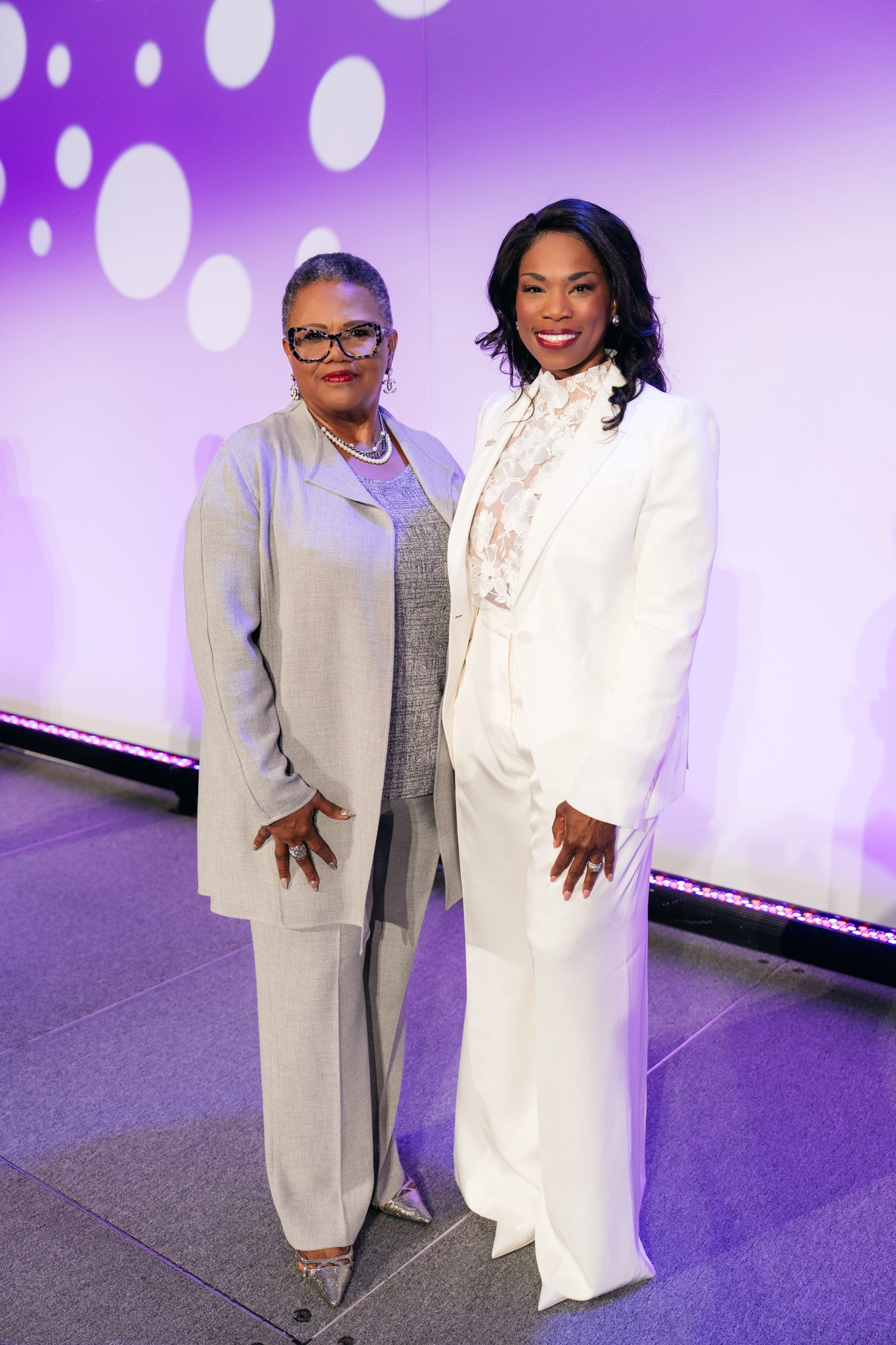 Reshema Kemps-Polanco (right) in white suit with mother at HBA professional event with purple backdrop