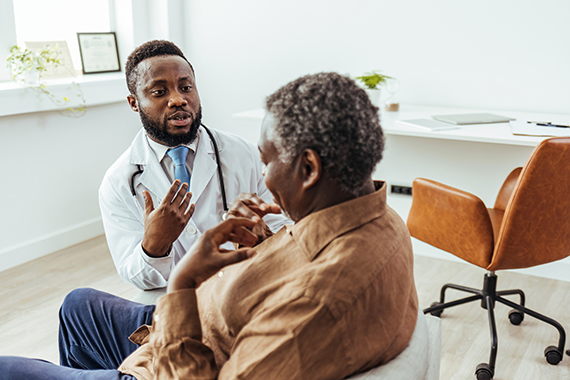 A doctor seated in his office, engaged in an earnest conversation with an older patient. The doctor gestures expressively as he explains information, while the patient listens intently, seated comfortably. The office environment is professional yet inviting.