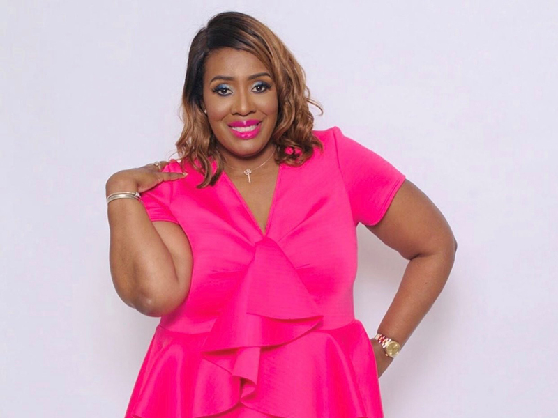 ShantaQuilette in bright pink dress, smiles and poses confidently with one hand on her hip