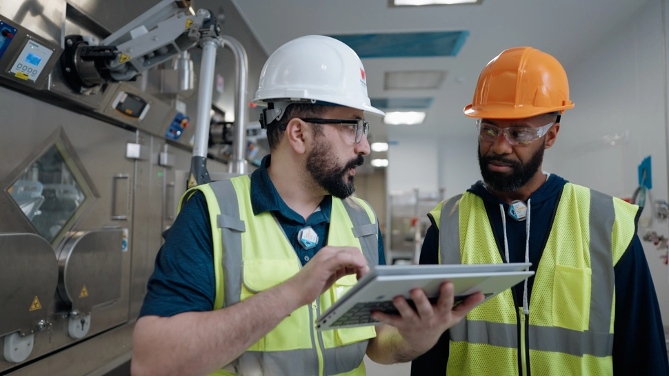 Two employees in hard hats talking in a manufacturing facility 