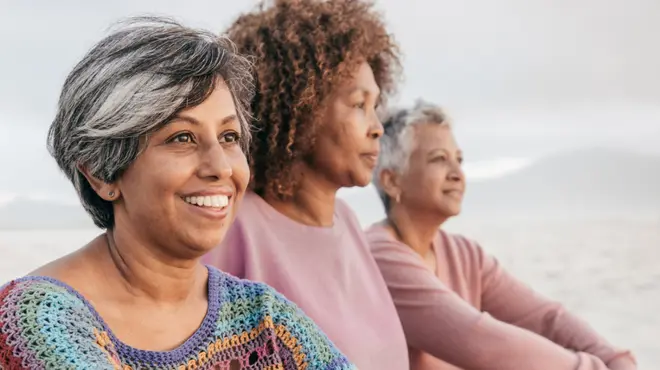 Three women sitting on a beach, looking out at the ocean.