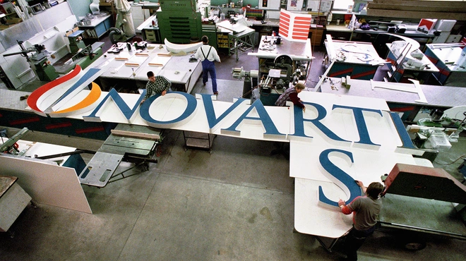 Several people working at assembling the big letters forming "Novartis" that will be installed at the top of a building on the Novartis Basel campus